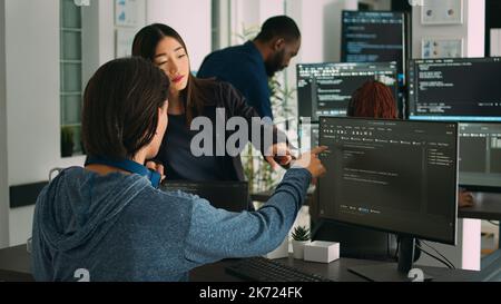 Asian database developers analyzing compiling code on multiple screens, working on new app interface development. System engineers using terminal window with firewall server data. Stock Photo