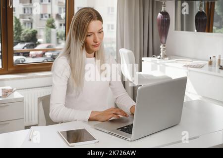 Woman works at the reception in a beauty salon. Typing something on laptop and talks on the phone with client, making appointments in studio Stock Photo