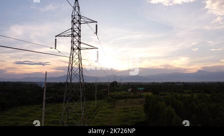 Aerial view of high voltage pylons and wires in the sky at sunset in the countryside. Drone footage of electric poles and wires at dusk. Stock Photo