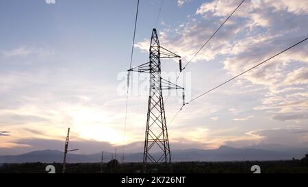 Aerial view of high voltage pylons and wires in the sky at sunset in the countryside. Drone footage of electric poles and wires at dusk. Stock Photo