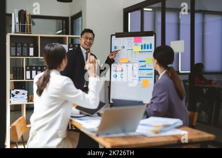 Business adviser explaining business plan strategy on flipchart to colleagues, male coach or adviser giving presentation at briefing, reporting about Stock Photo