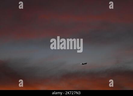 17 October 2022, Hesse, Frankfurt/Main: While a passenger plane is on approach to Frankfurt Airport, the sky is colored orange-red at sunrise in the early morning. Photo: Arne Dedert/dpa Stock Photo