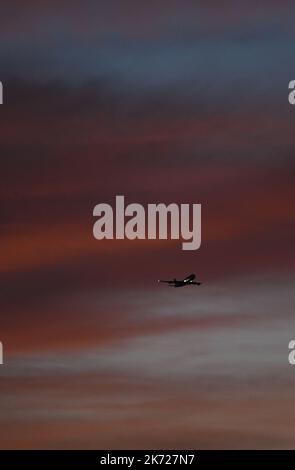 17 October 2022, Hesse, Frankfurt/Main: While a passenger plane is on approach to Frankfurt Airport, the sky is colored orange-red at sunrise in the early morning. Photo: Arne Dedert/dpa Stock Photo