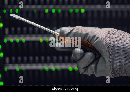 Screwdriver in the hands of a man at the server for data storage, close-up Stock Photo