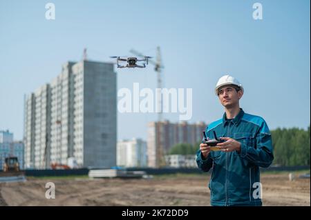 A man in a helmet and overalls controls a drone at a construction site. The builder carries out technical oversight. Stock Photo