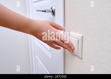 Woman reaches for the light switch, hand turns on the lamp close-up. White light switch in home room and man hand Stock Photo