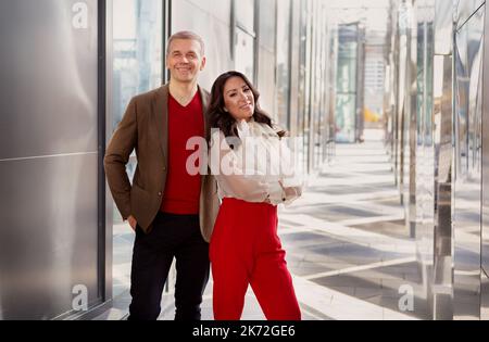 Successful cooperation multiethnic partners. Asian woman in stylish clothes (red pants, shirt), handsome causasian smiling man in business casual jack Stock Photo