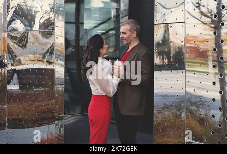 Attractive couple of colleagues talking and flirting near office . Business man and woman dating after work holding hands on street in fall, wearing s Stock Photo