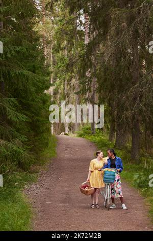 Female couple walking in forest with bicycle Stock Photo