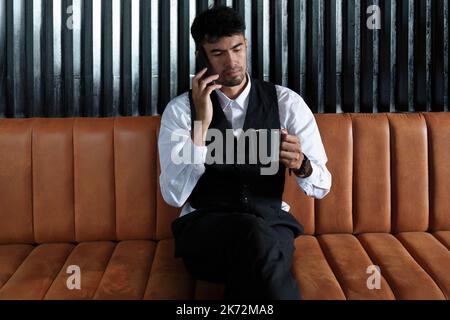 Portrait of a nice and discreet Asian man sitting on a sofa using a smartphone and drinking coffee Stock Photo