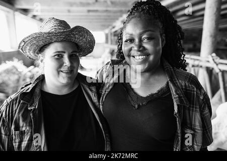 Multiracial young farmers working inside cowshed - Focus on african girl face - Black and white editing Stock Photo