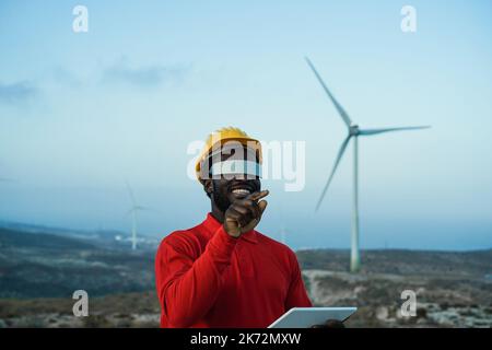 African engineer man using futuristic augmented reality glasses on a windmill farm - Focus on hand Stock Photo