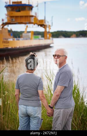 Senior couple holding hands and looking at industrial barge Stock Photo