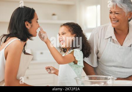 Just a quick little powder. a young girl playfully putting flour on her mothers nose during baking. Stock Photo