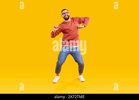 Happy funny young man in modern casual outfit dancing on yellow studio background Stock Photo