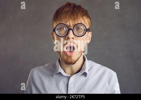 Studio headshot portrait of shocked young man in funny round glasses looking at camera Stock Photo