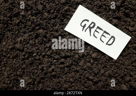 Greed or greedy concept. Paper note with handwritten word on dark soil grave background. Stock Photo