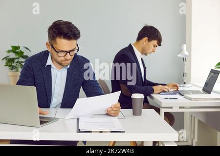 Two serious people sitting at their desks in the office and working with business documents Stock Photo