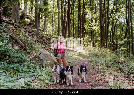 Senior woman walking with her three dogs in forest. Stock Photo