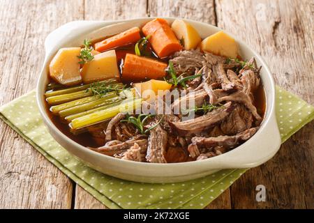 Slow cooked pot roast with carrots, celery, potatoes, garlic and gravy closeup in the bowl on the wooden table. Horizontal