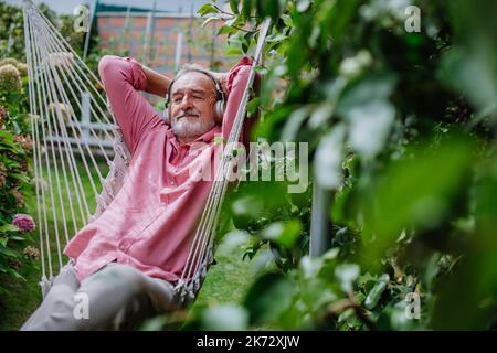 Happy senior man relaxing and listening music in outdoor swing,in his garden. Stock Photo