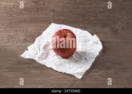 A wilted red apple on a crumpled tissue on a wooden table Stock Photo