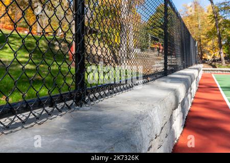 Interesting green and red outdoor basketball court at school playground.  Court includes retaining walls and black vinyl coated chain link fence. Stock Photo