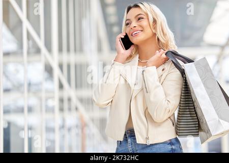 Youre going to love it. a young woman using her smartphone to make a phone call while shopping. Stock Photo