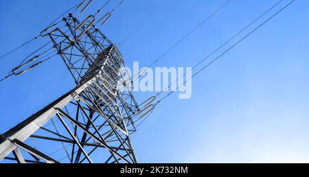 Steel power pylon construction with high voltage cables against clear blue sky and sun Stock Photo