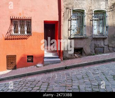 Exterior facade of old residential building with walls painted in orange, and wrought iron windows, at a narrow cobblestone street, Balat district, Istanbul, Turkey Stock Photo