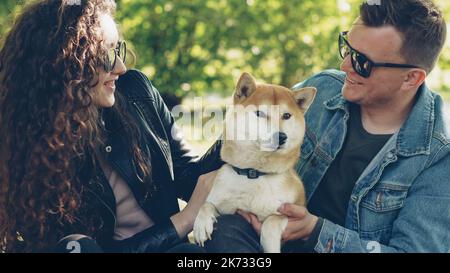 Husband and wife are are patting their favourite pet cute dog and laughing. Having fun with animals, loving puppies and youth concept. Stock Photo