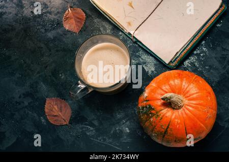 One pumpkin squash and a latte coffee made with with plant based oat soya or almond milk  with blank notepad notebook at the table on the dark black b Stock Photo