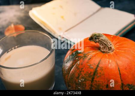 One pumpkin squash and a latte coffee made with with plant based oat soya or almond milk  with blank notepad notebook at the table on the dark black b Stock Photo
