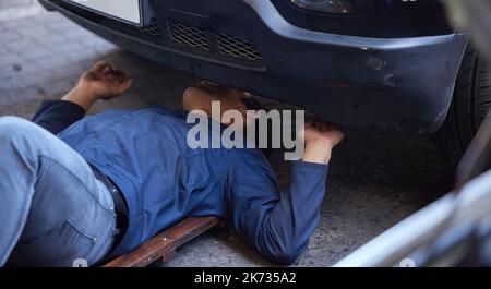 Checking every inch of your car. High angle shot of a handsome young male mechanic using a creeper while working on the engine of a car during a Stock Photo