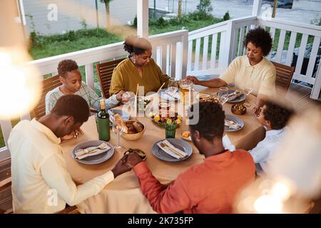 High angle view of African American family saying grace at dinner table outdoors and holding hands in cozy evening setting Stock Photo