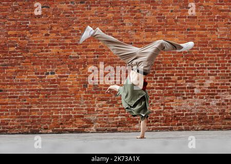 Motion shot of young man doing breakdance handstand pose against brick wall, copy space Stock Photo