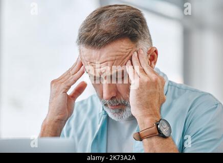 I cant get my head around this. a mature businessman sitting alone in his office and suffering from a headache while using his laptop. Stock Photo