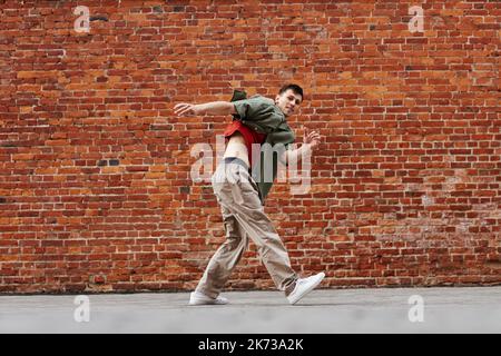 Motion shot of young man dancing hip-hop style outdoors against brick wall, copy space Stock Photo