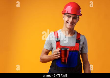 Young builder in uniform holding coffee cup on yellow background Stock Photo