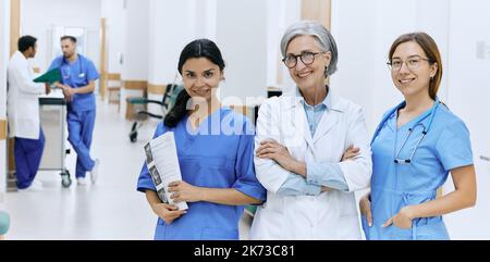 Multinational medical team. Portrait of mature chief physician with two nurses standing at corridor of hospital and looking at camera Stock Photo