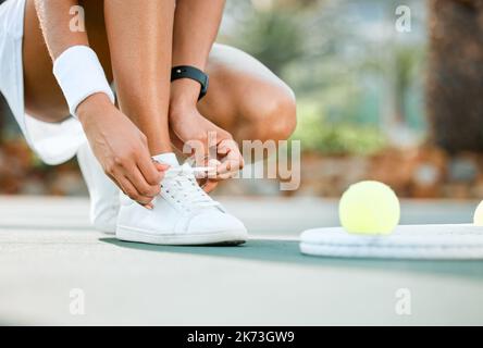 No tripping on this court. a sporty young woman tying her laces while playing tennis on a court. Stock Photo