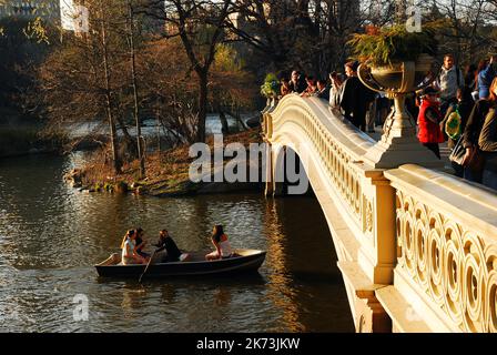 Couples enjoy a warm spring day in a rowboat on the lake in New York Central Park while people on the Bow Bridge take in the view Stock Photo