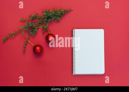 Soft Selective focus on Open blank spiral notebook near Christmas tree branch with decorations on trendy red background. Copy space text, to-do list, dreams. Planning 2023, writing Christmas wish list Stock Photo