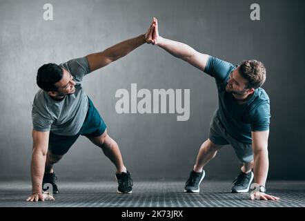 Weve got this. Full length shot of two handsome young male athletes high fiving while doing pushups side by side against a grey background. Stock Photo