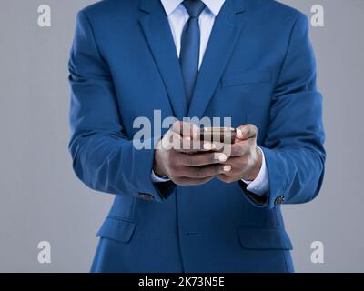 He never sends out mixed messages. an unrecognizable businessman checking his text messages in studio against a grey background. Stock Photo