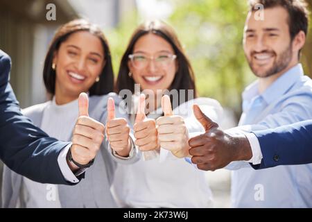 Hoping for rainbows ahead. Portrait of a group of young businesspeople showing a thumbs up outside. Stock Photo