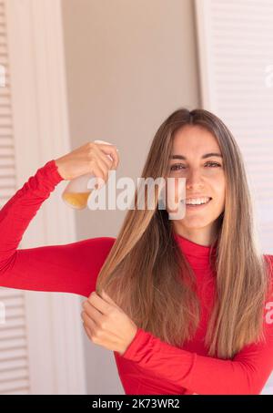Vertical view of young woman applying spray treatment in the shiny and beautiful blond long hair Stock Photo