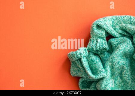 Green sweater on orange background, flat lay. Stock Photo