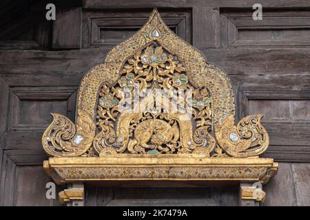 Closeup of beautiful ancient gilded wood carving panel above window of heritage landmark Wat Phan Tao buddhist temple facade, Chiang Mai, Thailand Stock Photo