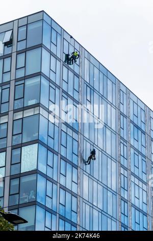 Two men suspended on ropes cleaning the windows of a high-rise apartment block, London, UK Stock Photo